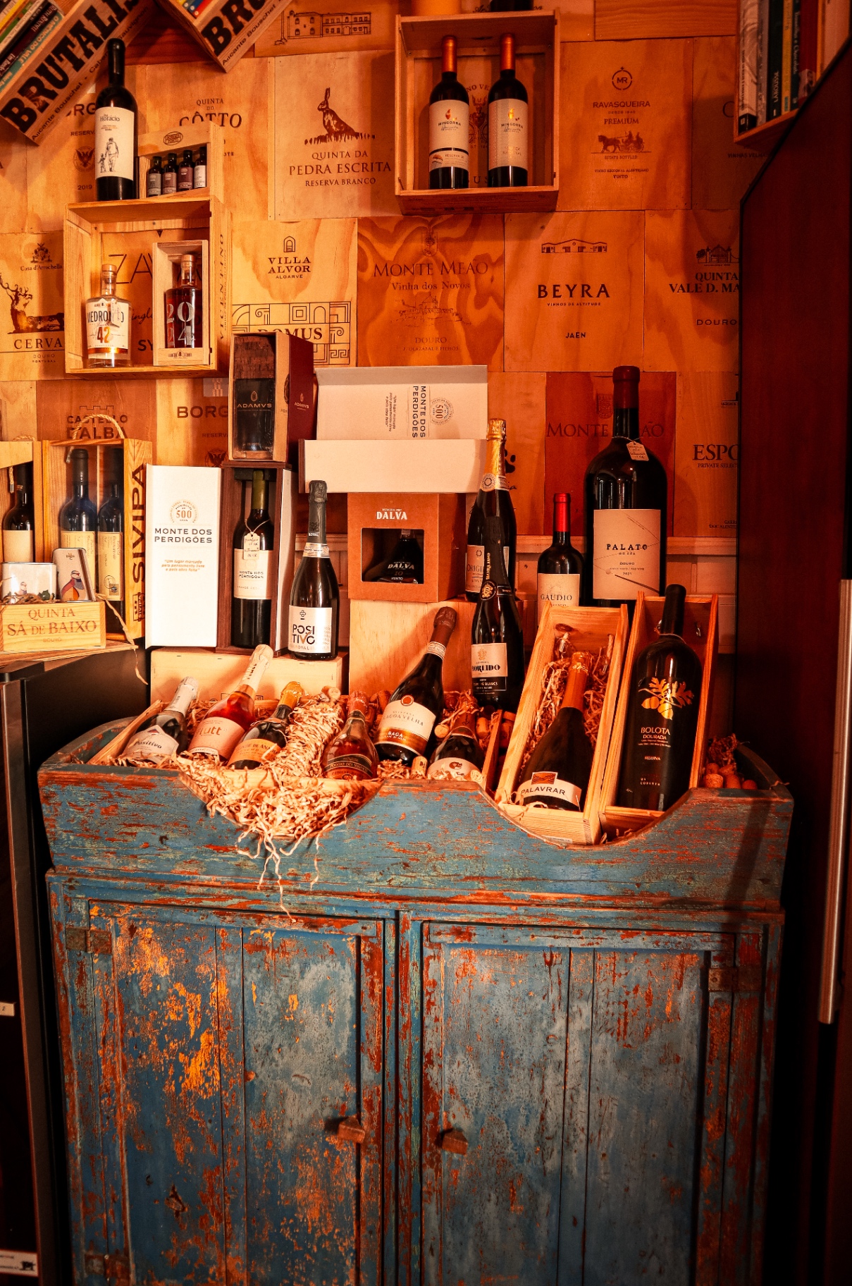 Cómoda azul com garrafas e parede de caixas de vinho
